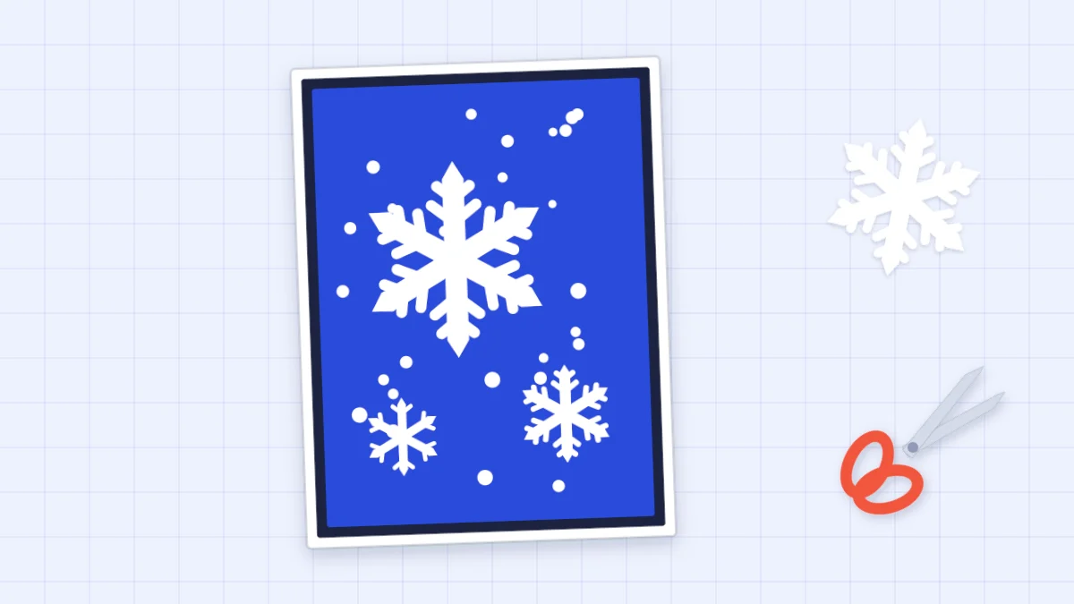 A handmade winter card with white paper snowflakes and snow dots on a blue panel, beside small scissors